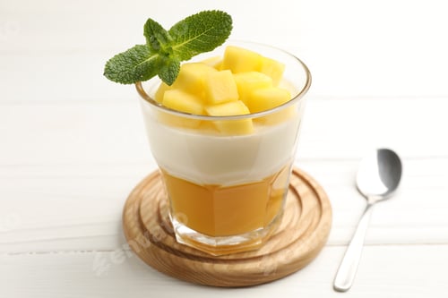Preview: Delicious mango panna cotta with mint and spoon on white wooden table, closeup