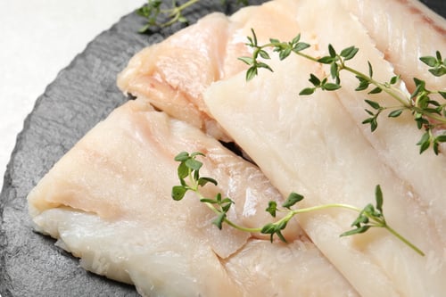 Preview: Pieces of raw cod fish and microgreens on table, closeup