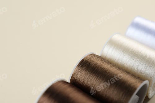 Preview: Spools of sewing threads on beige background, closeup. Space for text