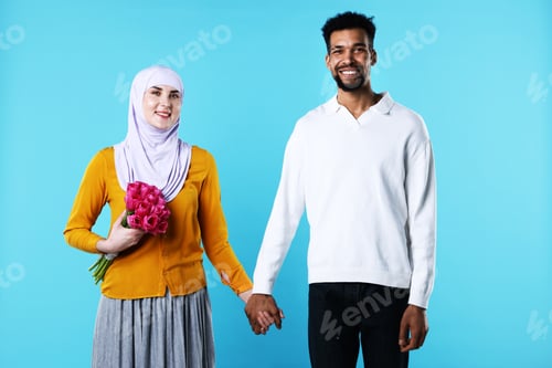 Preview: Portrait of happy muslim couple with beautiful tulips holding hands on light blue background