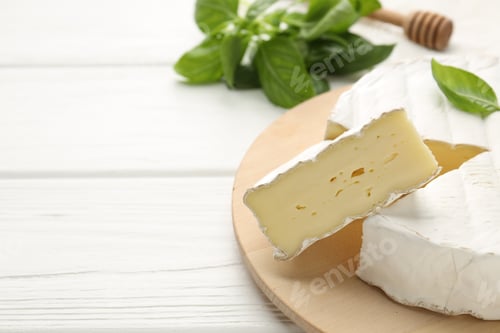 Preview: Cut delicious brie cheese and basil on white wooden table, closeup. Space for text