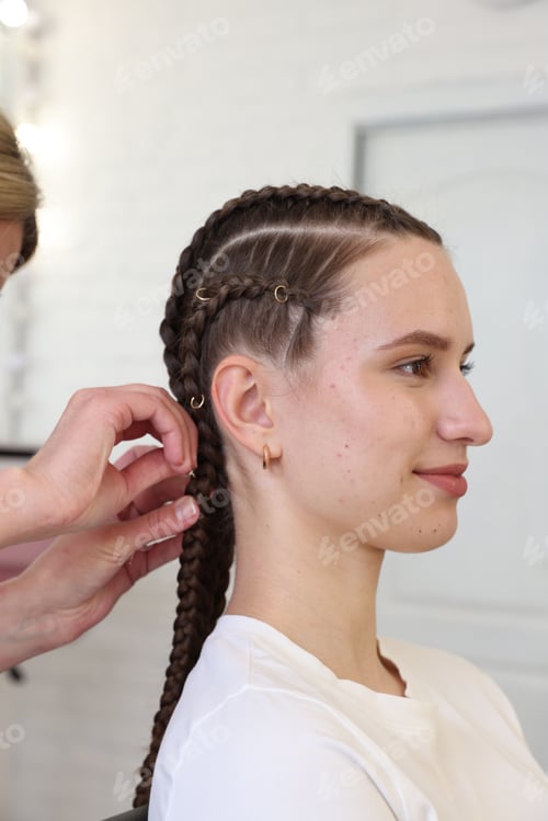 Preview: Hairstylist braiding teenage girl's hair in salon, closeup