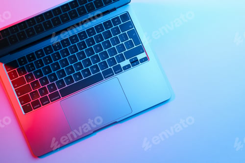 Preview: Modern laptop in neon lights on light table, top view. Space for text