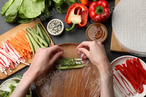 Preview: Making spring rolls. Woman wrapping rice paper with ingredients at dark table, top view