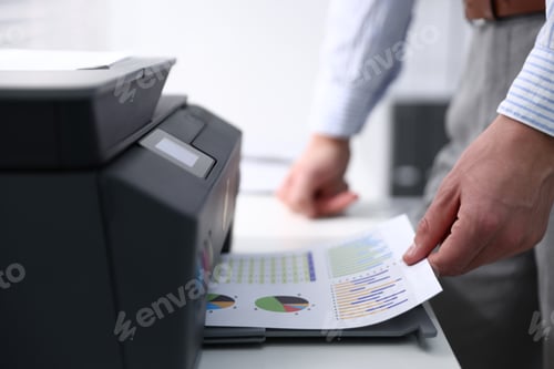 Preview: Man taking printed sheet of paper from printer at white desk indoors, closeup