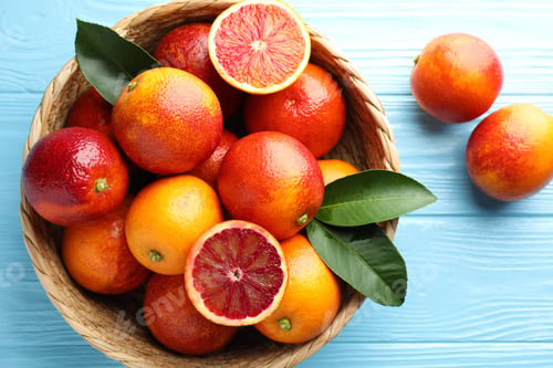 Preview: Juicy Sicilian oranges and green leaves in wicker basket on light blue wooden table, flat lay