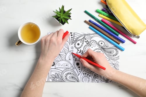 Preview: Woman coloring antistress picture with felt tip pen at white table, top view