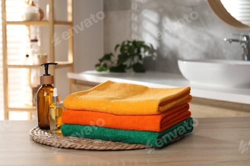 Preview: Stack of colorful towels and cosmetic products on wooden table in bathroom