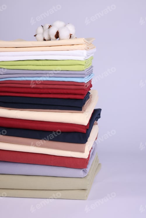 Preview: Stack of colorful bed linens and cotton flowers on white background, closeup
