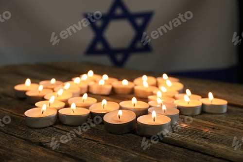 Preview: Holocaust Remembrance Day. Burning candles in shape of Star of David on wooden table against flag of