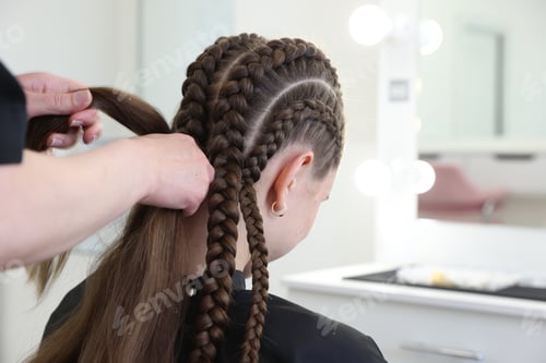Preview: Hairstylist braiding teenage girl's hair in salon, closeup