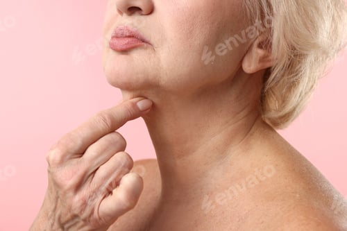 Preview: Senior woman touching her neck on light pink background, closeup