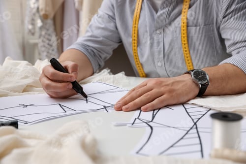 Preview: Dressmaker working with sewing pattern at white table in atelier, closeup