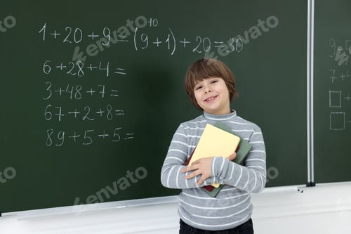 Preview: Schoolboy with notebooks near chalkboard with math assignment in classroom