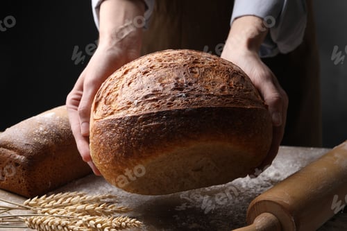 Preview: Woman with loaf of fresh bread at wooden table, closeup