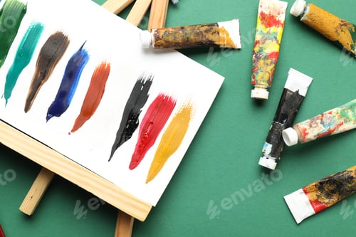 Preview: Tubes with watercolor paints and painting on green background, flat lay