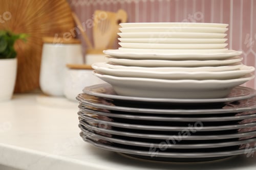 Preview: Set of clean plates and utensils on white countertop in kitchen, closeup. Space for text