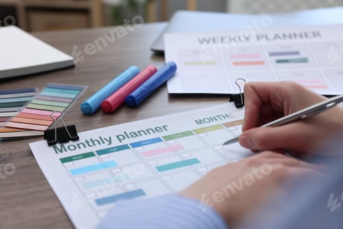 Preview: Woman with monthly planner at wooden desk, closeup
