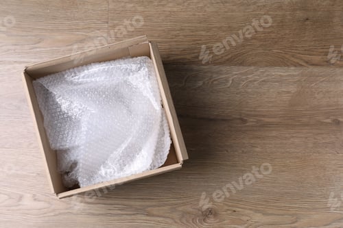 Preview: Bubble wrap in cardboard box on wooden table, top view. Space for text