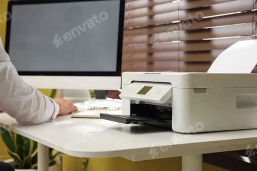 Preview: Man working on computer near printer at white desk indoors, closeup