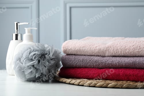 Preview: Stack of colorful terry towels, sponge and cosmetic products on table near light wall
