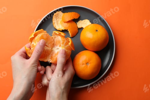 Preview: Woman peeling ripe tangerine and fresh fruits on orange background, top view