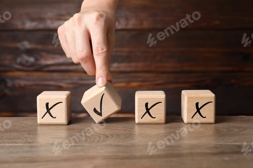 Preview: Woman putting cube with checkmark next to others with cross marks on wooden table, closeup. Followin