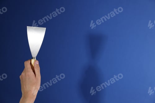 Preview: Handyman with putty knife on blue background, closeup. Space for text