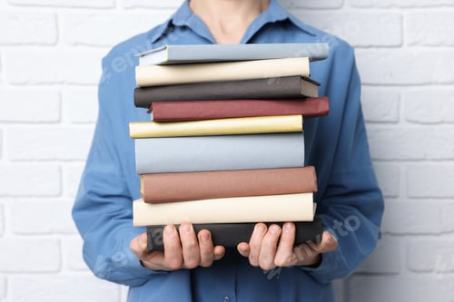 Preview: Woman holding stack of different books near white brick wall, closeup