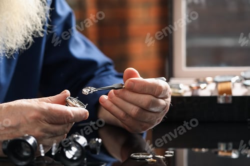 Preview: Senior man fixing mechanism of vintage wrist watch at black mirror table indoors, closeup