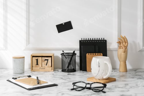 Preview: Stylish office workplace. Decor elements, glasses, cup and stationery on marble table near white wal