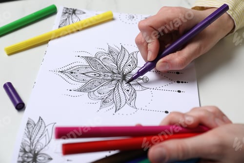Preview: Woman coloring antistress picture with felt tip pen at white table, closeup