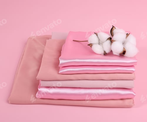 Preview: Stack of fresh bed linens and cotton flowers on pink background, closeup