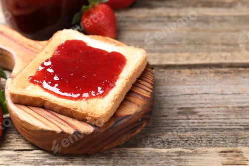 Preview: Toasted bread with strawberry jam on wooden table, closeup. Space for text
