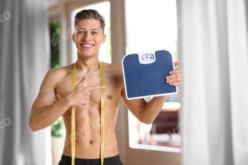 Preview: Happy man with measuring tape pointing at bathroom scale in room. Weight loss result