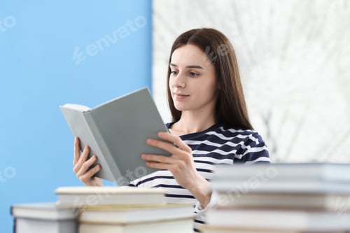 Preview: Young woman reading book and stacks of colorful ones at home