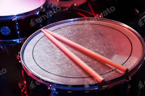 Preview: Wooden drumsticks on drum in color light, closeup