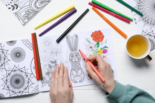 Preview: Woman coloring antistress picture with felt tip pen at white table, top view