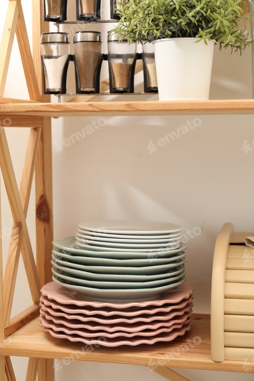 Preview: Set of clean plates, spices, plant and breadbox on wooden shelves in kitchen, closeup