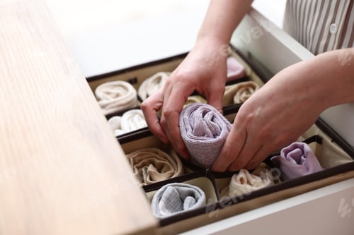 Preview: Woman putting socks into drawer with organizer indoors, closeup