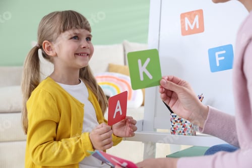 Preview: Mother teaching her daughter alphabet with letter cards at home, closeup