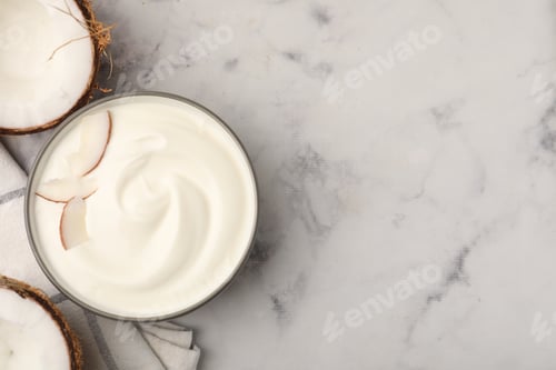 Preview: Delicious coconut yogurt with flakes in bowl and halves of fruit on grey marble table, flat lay. Spa