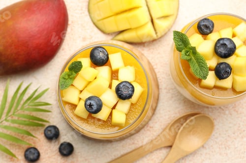 Preview: Delicious mango panna cotta with fruits and mint in glasses on beige textured table, flat lay
