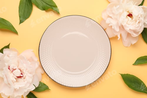 Preview: Stylish table setting with plate, flowers and green leaves on pale orange background, flat lay
