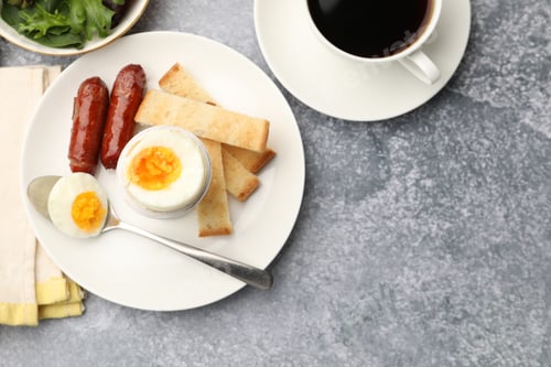 Preview: Tasty breakfast with hard boiled egg served on grey table, flat lay. Space for text