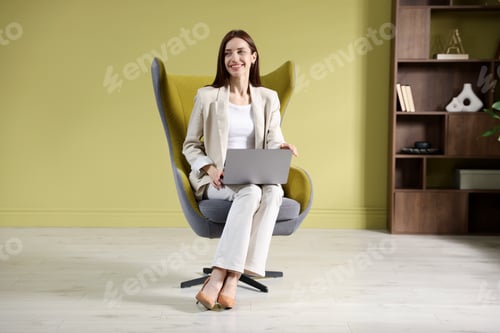 Preview: Happy woman using laptop in armchair indoors