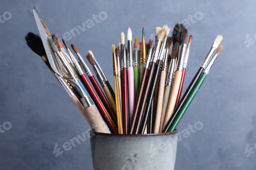 Preview: Different paintbrushes in holder on blue background, closeup