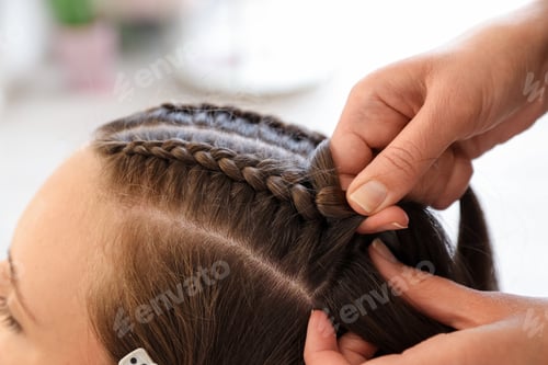 Preview: Hairstylist braiding teenage girl's hair in salon, closeup