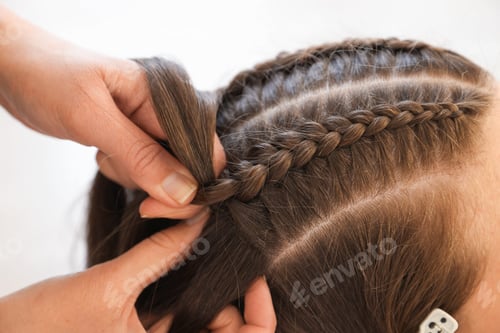 Preview: Hairstylist braiding teenage girl's hair against light background, closeup