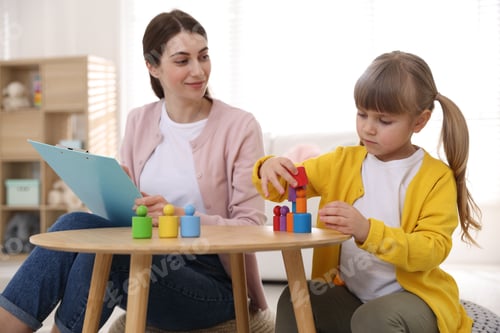 Preview: Professional psychologist working while little girl playing with toys at wooden table indoors
